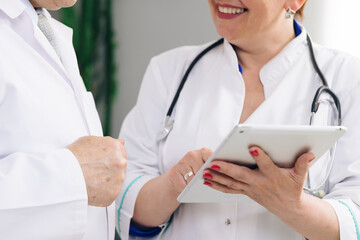Closeup view of man and woman doctors using tablet during working day at clinic. Caucasian person and his female colleagues use electronic device and work together while standing indoors.