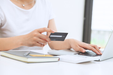 A woman sits in the house with a laptop and holds a credit card to shop online. The concept of online shopping
