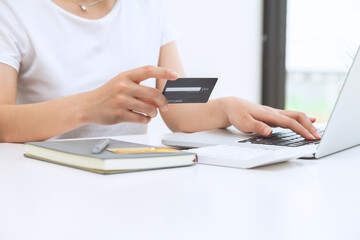 A woman sits in the house with a laptop and holds a credit card to shop online. The concept of online shopping
