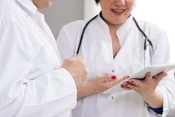 Caucasian person and his female colleagues use electronic device and work together while standing indoors. Closeup view of man and woman doctors using tablet during working day at clinic