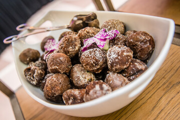 Brown powdered donut holes in serving bowl with purple flower. Macro view