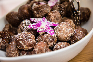 Brown powdered donut holes in serving bowl with purple flower. Macro view