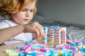 Small cute preschooler girl playing with colorful toy building blocks, sitting at the table.