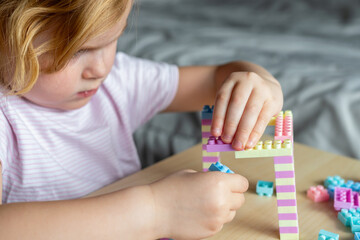 Small cute preschooler girl playing with colorful toy building blocks, sitting at the table.