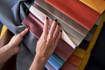 Choosing upholstery fabric color and texture from various colorful samples in a store. Female customer hands touching textile.