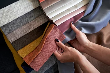 Poster Im Rahmen Choosing upholstery fabric color and texture from various colorful samples in a store. Female customer hands touching textile. © berezko