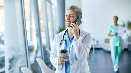Happy healthcare worker communicating over mobile phone during her coffee break at medical clinic.