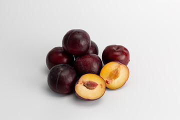 several plums and one cut in half on a white background