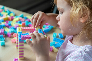 Small cute preschooler girl playing with colorful toy building blocks, sitting at the table.