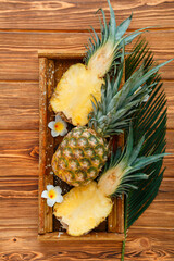 Ripe Pineapple. Tropical summer fruit pineapple halves and whole pineapple on brown dark table in wooden box with tropical plumeria flowers. Top view