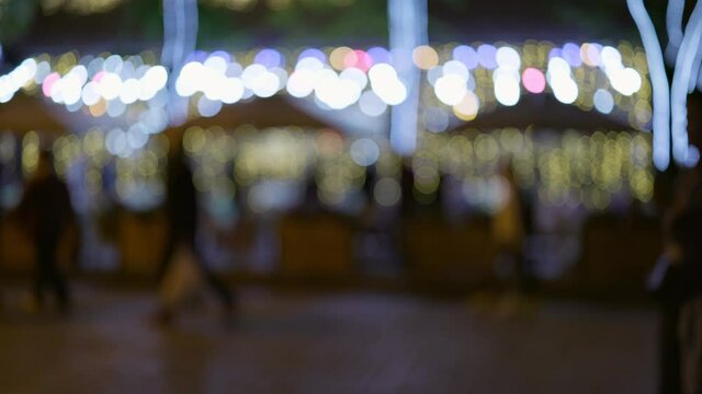 People walk in the evening city with multi-colored illumination. Unrecognizable silhouettes of people on the background of cafes and restaurants with backlight. Night city life concept, 4K
