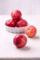 Red plum in a white ceramic bowl on a table with a light linen tablecloth. Healthy organic harvest. Vertical photo