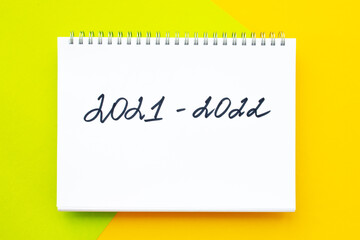 Handwriting inscription in white notepad, on vivid yellow - green background. 2021-2022 New school academic year. Flat lay, top view. Back to school concept.