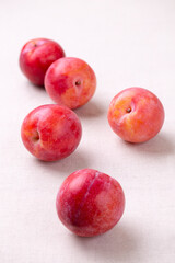 Red plum is scattered on the table with a light linen tablecloth. Healthy organic harvest. Vertical photo