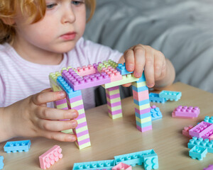 Small cute preschooler girl playing with colorful toy building blocks, sitting at the table.