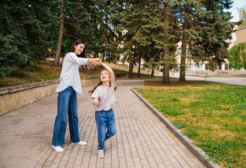 Fototapeta premium A young mother and her little daughter are dancing in the park. A girl and a woman are circling on the sidewalk.