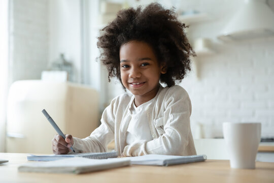 Portrait of smiling little African American girl child feel excited study learn at home kitchen. Happy small 8s biracial ethnic kid do homework assignment in notebook. Education, diversity concept. - Powered by Adobe