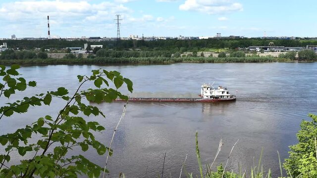 A river push boat carries a barge loaded with sand on the river in summer. High quality 4k footage