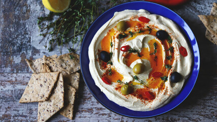 Hummus with olives, paprika and olive oil in a blue plate. A traditional Middle Eastern snack.
