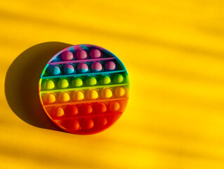 Trendy colorful anti-stress sensory toy. Silicone fidget push pop it for fine motoric skills lies in the sun. Flat lay on yellow background. Picture with place for text.