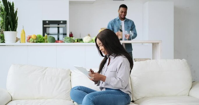 African American couple drinking wine while using tablet at home