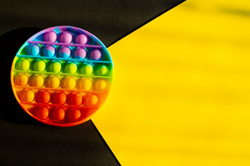 Trendy colorful anti-stress sensory toy. Silicone fidget push pop it for fine motoric skills lies in the sun. Flat lay on yellow and plack background. Picture with place for text.