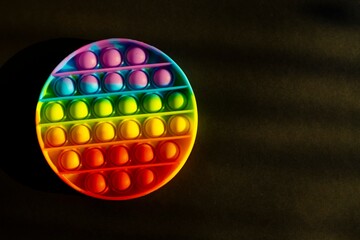 Trendy colorful anti-stress sensory toy. Silicone fidget push pop it for fine motoric skills lies in the sun. Flat lay on black background. Picture with place for text.