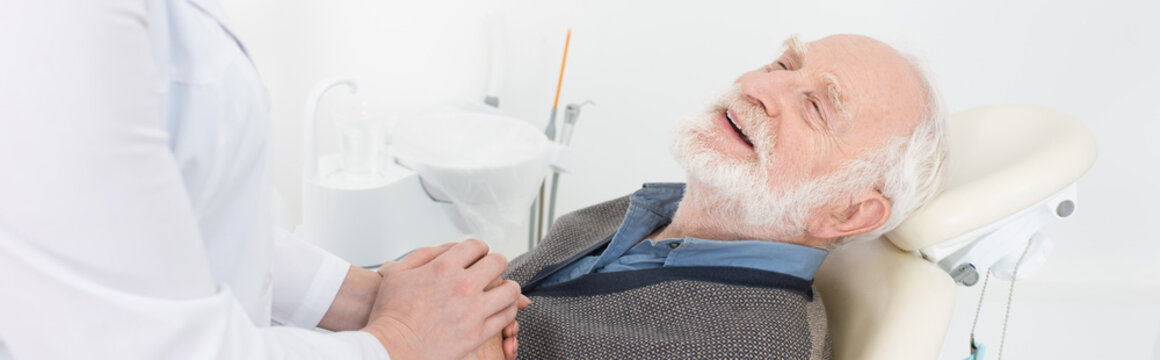 Grateful Elderly Patient In Dental Chair Holding Hands With Dentist, Banner.