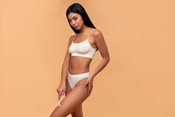 Young Asian woman in white lingerie with a straight razor on a beige background. Depilation, body care.