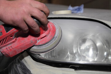 Car headlight buff with vibration pollishing machine in serviceman hand closeup, vehicle body repair service