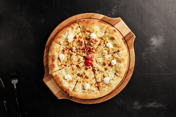 pizza on a wooden base on a black textured background top view