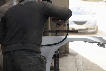 Service man paints a car body part new fender with ground painting gun on holding frame device, vehicle body repair garage service