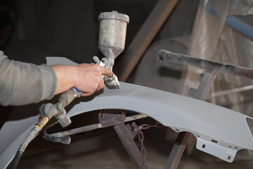 Service man hand paints a car body part new fender with ground painting gun on holding frame...
