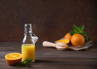 Fresh orange juice in bottle with citrus fruits  and mint  on a brown wooden background. Healthy and diet drink. Front view and copy space