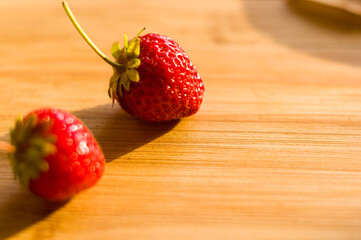 Ripe fresh strawberries on bamboo wooden background with long shadow, close up.