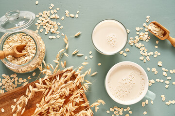 Oat milk in a glass and mug on a blue background. Flakes and ears for oatmeal and granola on a wooden plate. - 435914854