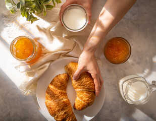In the photo, two mouth-watering croissants lie on a white plate. Orange jam, milk in glass...