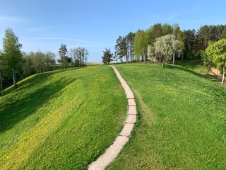 Fototapeta na wymiar Spring meadow with hiking trail, trees, hill and blue sky.
