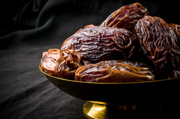 Big luxury dried date fruit in bowls on the dark surface, kurma ramadan kareem concept, close up.