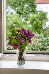 Close up of a vase with beautiful purple lilac flowers at the window