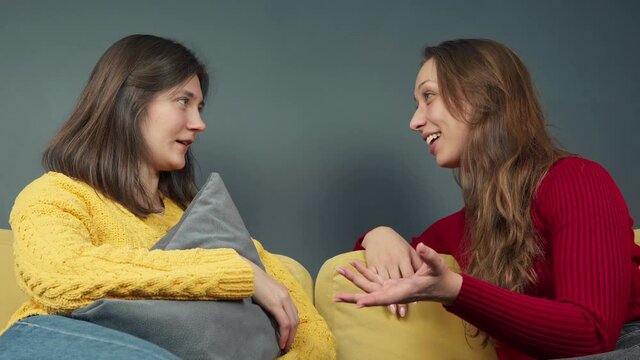 Two smiling girls discussing gossip sitting on cozy yellow sofa girls make high-five gesture. People relations concept. female friendly gathering. Girlfriends roommates chatting about friends