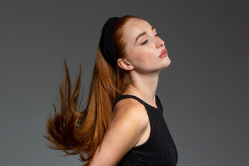 Beautiful young woman with ginger, red hair in black dress in studio