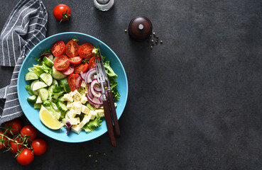 Mix salad with vegetables, leaves and feta. Greek salad in a plate on a blue concrete background. View from above.