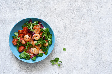 Mix salad with shrimps, tomatoes and leaves in a blue plate on the kitchen table. View from above.