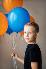 Fototapeta na wymiar A boy of European appearance in a black T-shirt stands with balloons.
