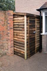 Wooden shed newly constructed as a tool shed or log storage area built against a brick surrounding wall.