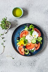Appetizing salad with feta cheese, fresh vegetables (tomatoes, cucumbers, onions), crispy lettuce, microgreens and violet flowers. Non-standard serving of Greek salad. Food with flowers
