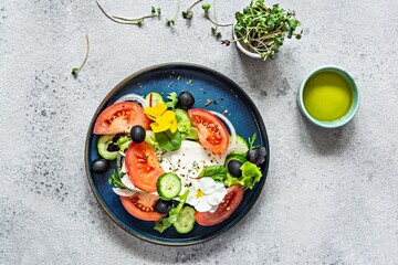 Appetizing salad with feta cheese, fresh vegetables (tomatoes, cucumbers, onions), crispy lettuce, microgreens and violet flowers. Non-standard serving of Greek salad. Food with flowers