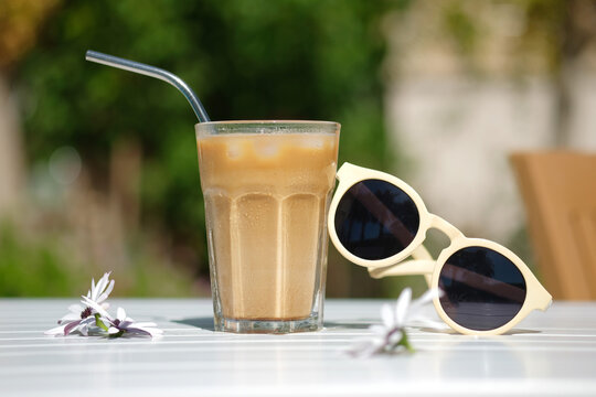 Ice coffee Cyprus Frappe Fredo side view on white table, with sunglasses. Summer minimalistic background, holiday or vacation concept. Sun and shadows