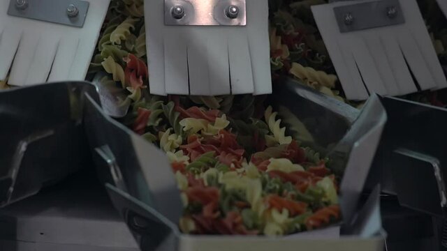 Close shot of a different colored macaroni moving to a packing machine. Industrial weighing-machine takes an equal number to every developing package